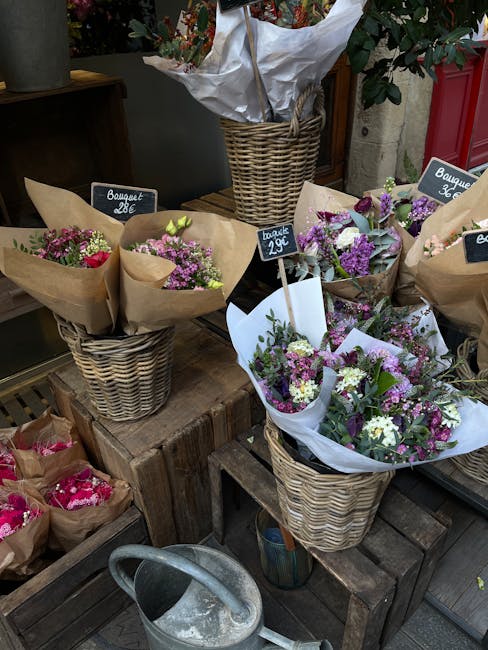 A display of fresh flower bouquets arranged in woven wicker baskets at a florist shop. The bouquets feature a mix of purple, white, and pink flowers, such as lilacs, spray roses, and asters, wrapped i